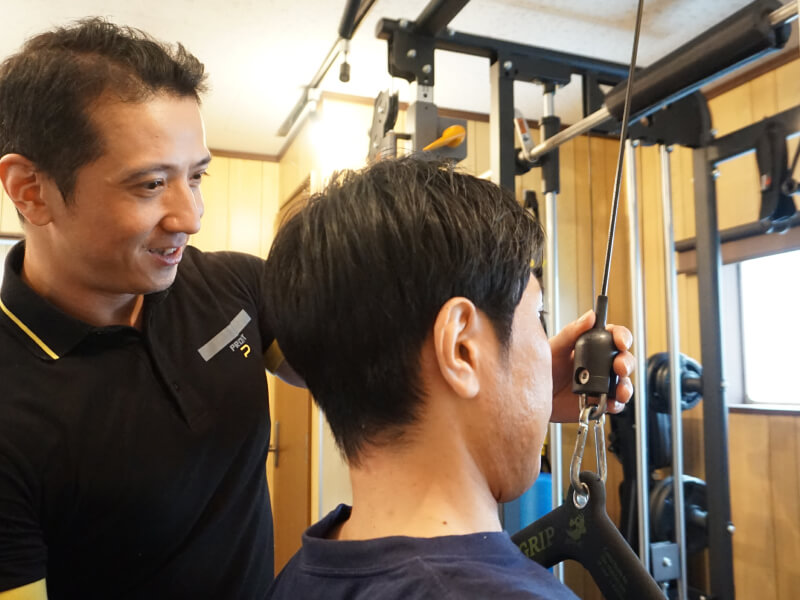 トレーナーが男性にトレーニングマシンの使い方を教えている。