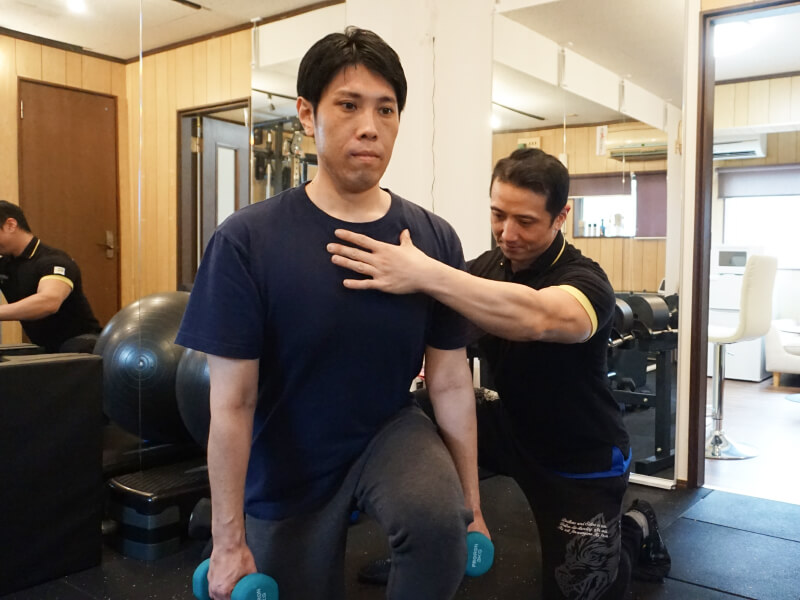 トレーナーが男性にダンベルを使ったランジのエクササイズを指導している。